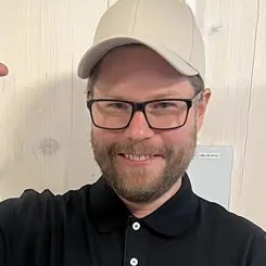 Stian Glomsrød smiler mot kamera, i svart pikéskjorte og caps
